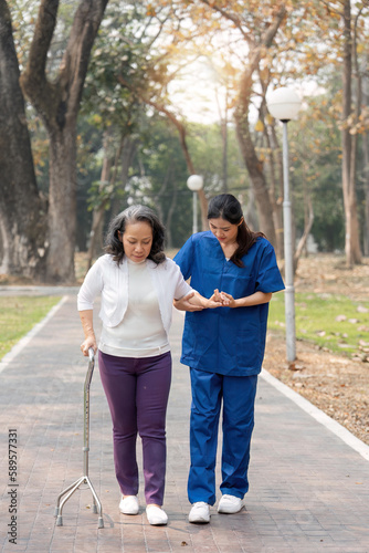 nurse helping elderly woman with walker Nurse holding hand and help elderly woman walking in park facility