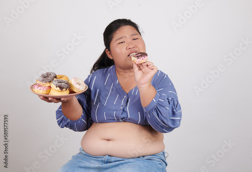 Happy fat woman eating donuts on plate isolated on color background. Food addiction  diet breakdown  eating disorders  depression  laziness problem eating  compulsive overeating concept.