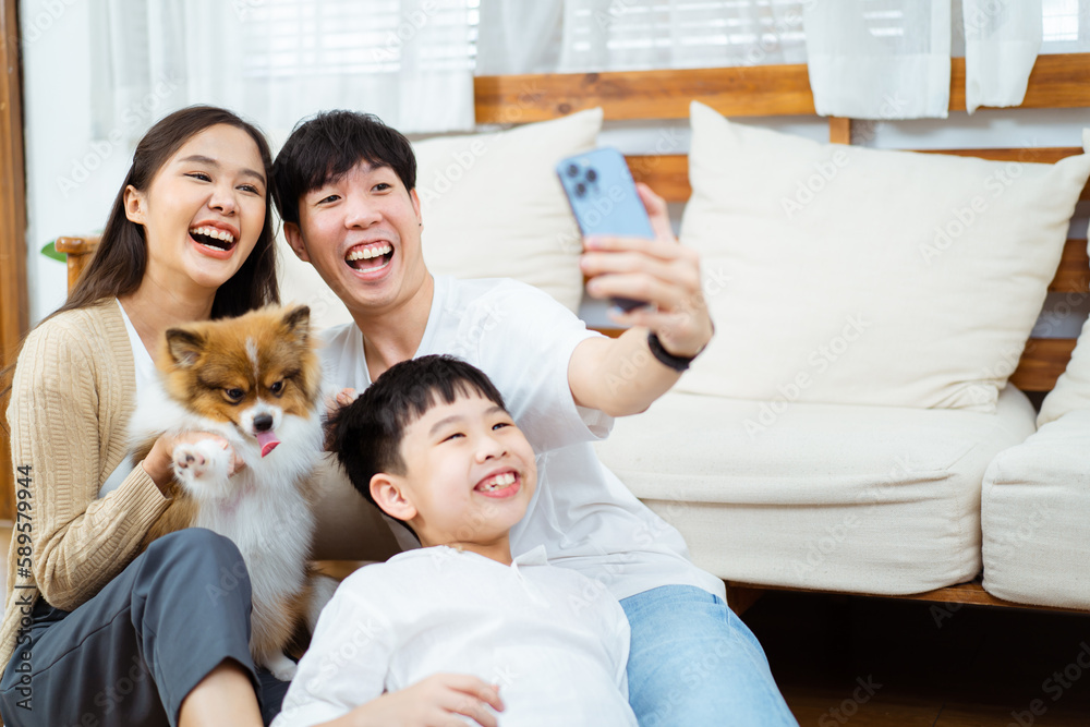 Happy cheerful Asian young couple taking a selfie photography or making a selfie video call on smartphone with their little dog in living room. Man and woman smiling to camera on smartphone. Happy cheerful Asian young couple taking a selfie photography or making a selfie video call on smartphone with their little dog in living room. Man and woman smiling to camera on smartphone.