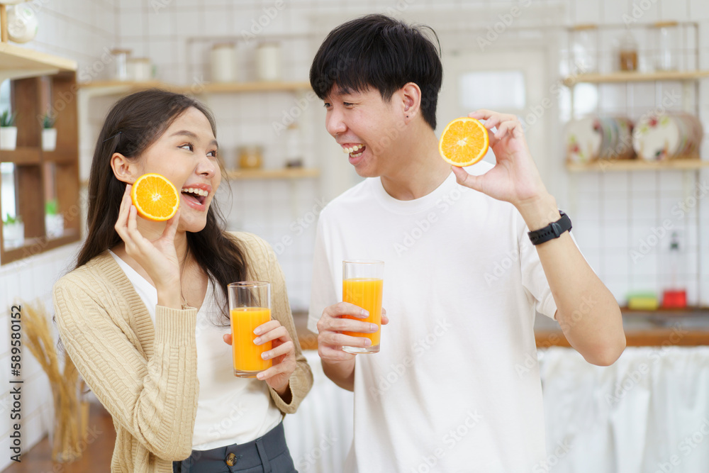 Happy cheerful Asian man and woman showing a half round of a fresh orange fruit to camera together and smiling. Happy cheerful Asian man and woman showing a half round of a fresh orange fruit to camera together and smiling.