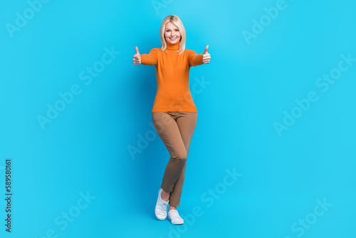 Full size photo of satisfied good mood woman wear orange turtleneck brown trousers showing thumbs up isolated on blue color background