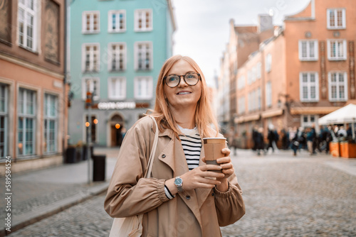 Young smiling woman in coat with coffee cup in evening city street in Gdansk old town. Traveling Europe in autumn. High quality photo © Shi 