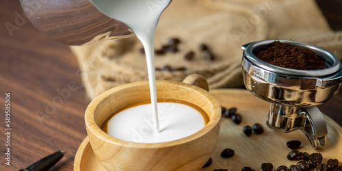 Hot coffee espresso latte with milk froth foam in wood cup. barista pouring milk liquid froth foam to wood cup of espresso for make creamy cappuccino hot drink. photo