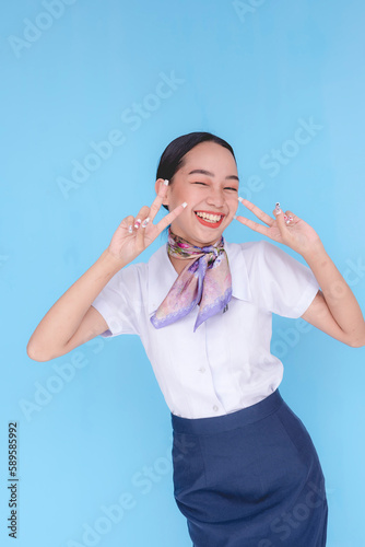 A flight attendant is smiling towards the camera while winking and doing the peace sign with both hands.