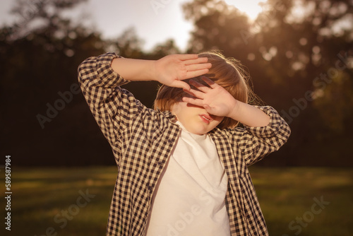 Photophobia Light Sensitivity content. Boy covering eyes by hand from sunlight outdoors. Sun Damage to Eyes Reversible photo