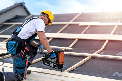 The carpenter nails a timber board using an electric nailer while working on a roof.