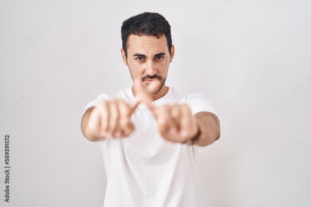 Handsome hispanic man standing over white background rejection expression crossing fingers doing negative sign Handsome hispanic man standing over white background rejection expression crossing fingers doing negative sign