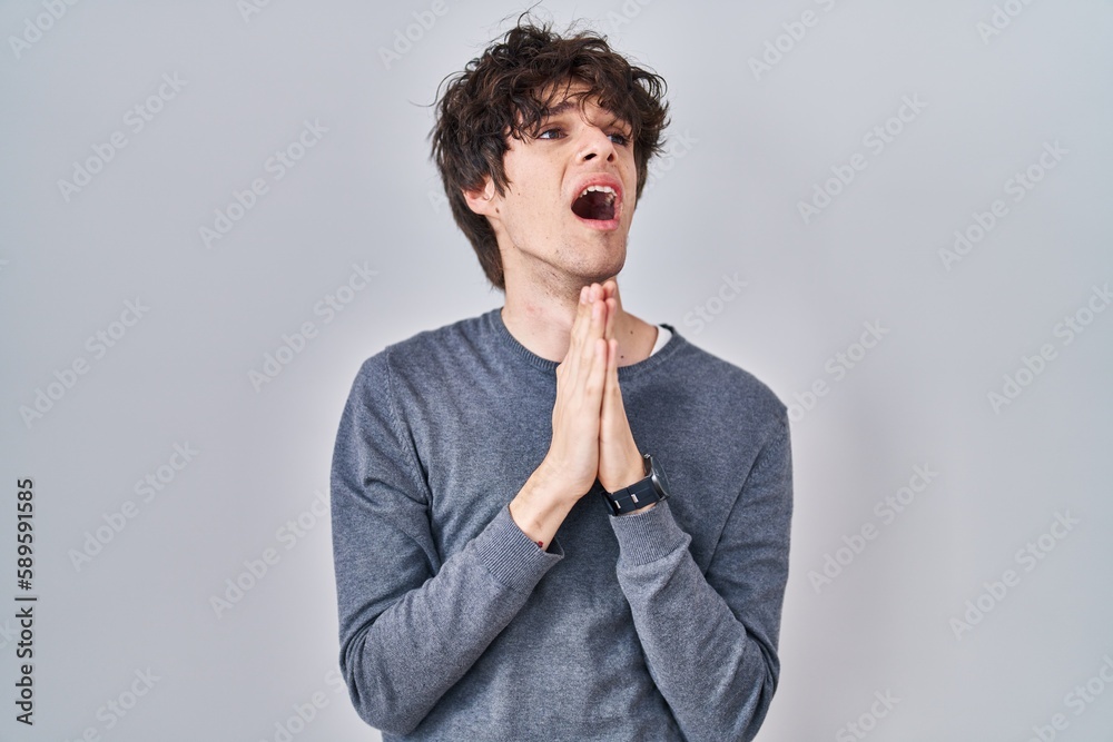 Young man standing over isolated background begging and praying with hands together with hope expression on face very emotional and worried. begging.