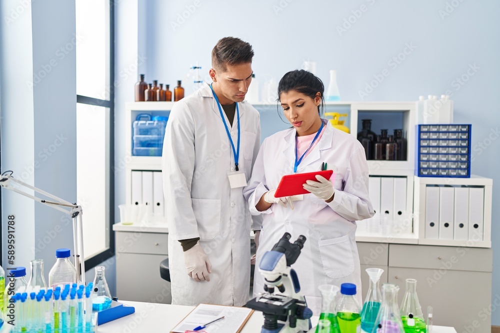 Man and woman scientists partners using touchpad at laboratory Man and woman scientists partners using touchpad at laboratory