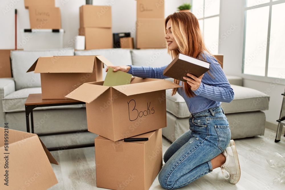 Young caucasian woman smiling confident putting books on cardboard box at new home Young caucasian woman smiling confident putting books on cardboard box at new home