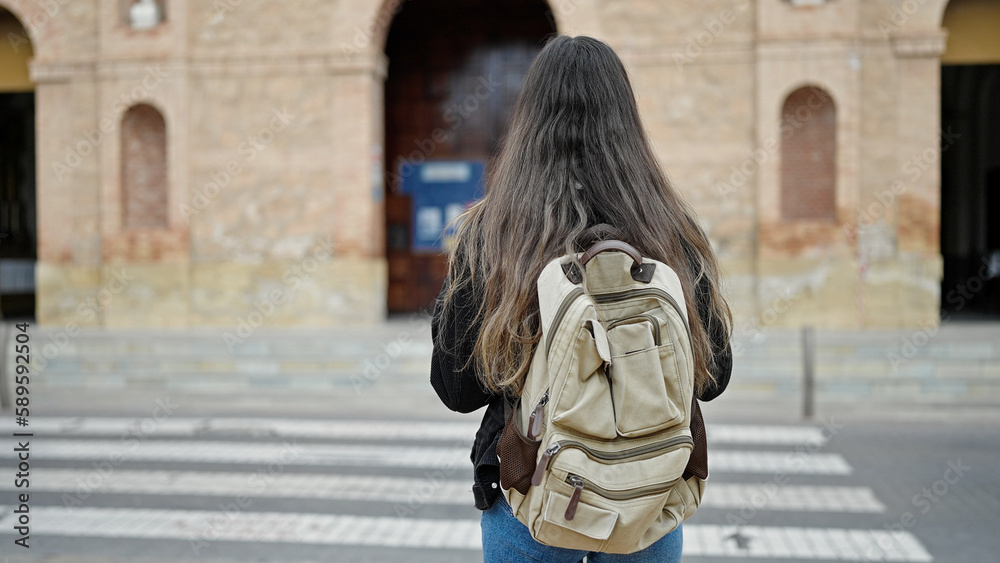 Young beautiful hispanic woman student standing on back view at street
