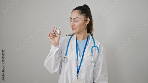 Young beautiful hispanic woman doctor holding pills over isolated white background