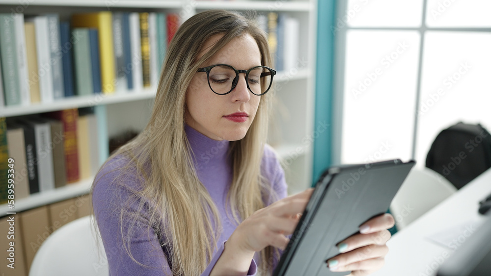 Young blonde woman student using touchpad studying at library university Young blonde woman student using touchpad studying at library university