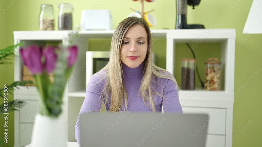 Young blonde woman using laptop sitting on table at home