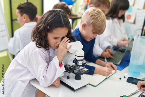 Group of kids students using microscope writing on notebook at laboratory classroom