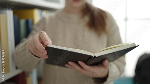 Young blonde woman student reading book at library university