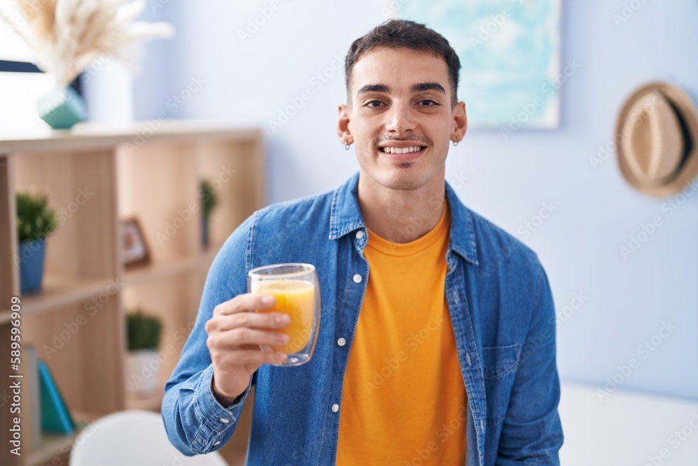 Handsome hispanic man drinking glass of orange juice looking positive and happy standing and smiling with a confident smile showing teeth Handsome hispanic man drinking glass of orange juice looking positive and happy standing and smiling with a confident smile showing teeth