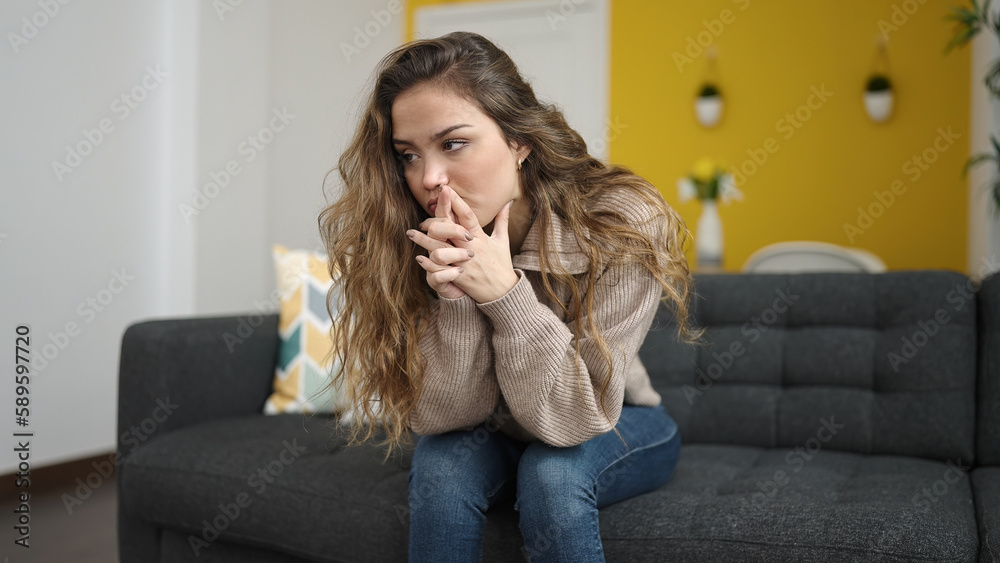 Fototapeta premium Young beautiful hispanic woman sitting on sofa with serious expression at home