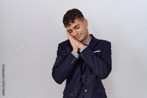 Young hispanic business man wearing suit and tie sleeping tired dreaming and posing with hands together while smiling with closed eyes.