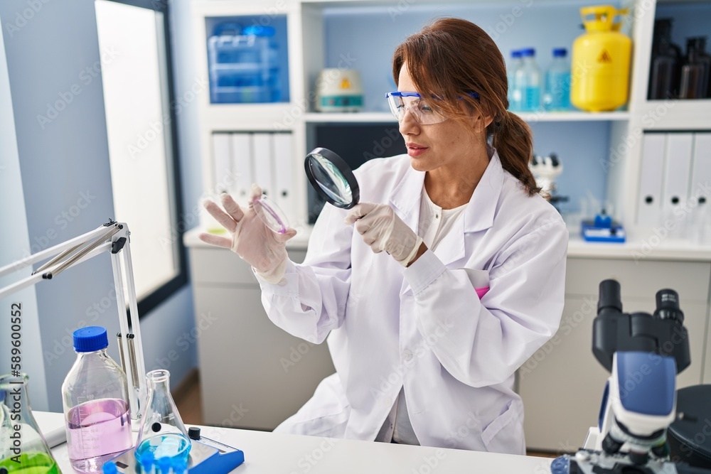 Young latin woman wearing scientist uniform using loupe at laboratory Young latin woman wearing scientist uniform using loupe at laboratory
