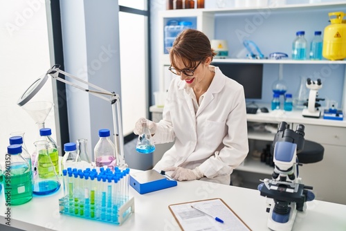 Young caucasian woman wearing scientist uniform measuring liquid at laboratory