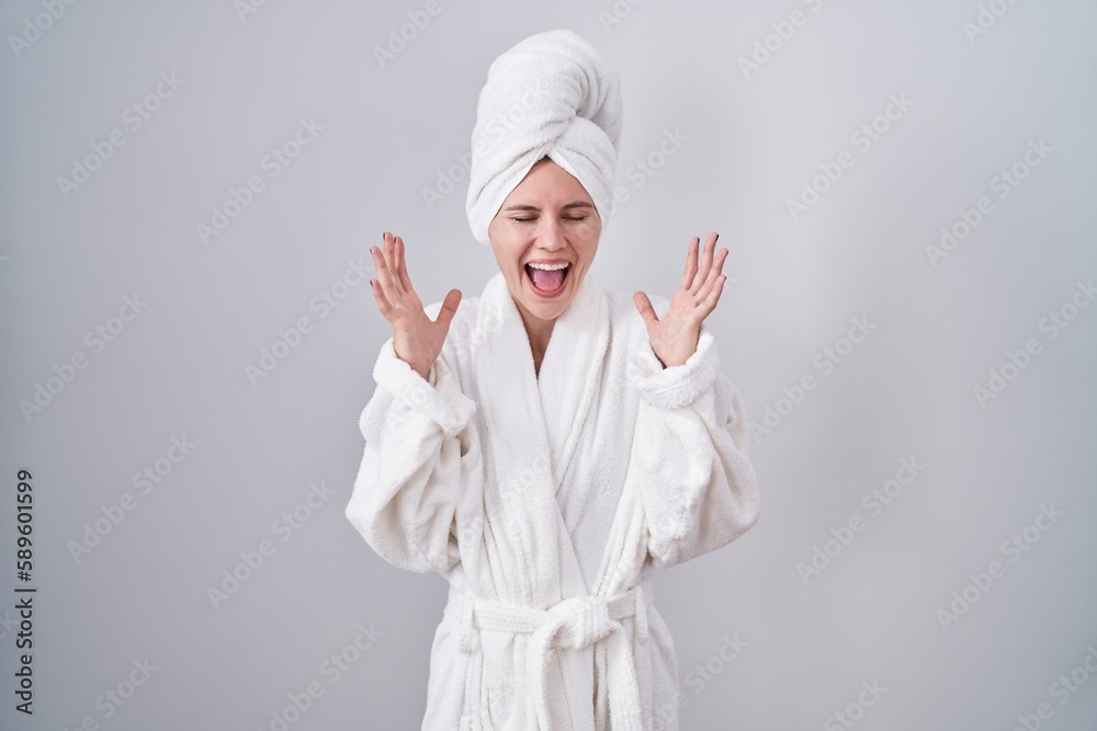 Blonde caucasian woman wearing bathrobe celebrating mad and crazy for success with arms raised and closed eyes screaming excited. winner concept Blonde caucasian woman wearing bathrobe celebrating mad and crazy for success with arms raised and closed eyes screaming excited. winner concept