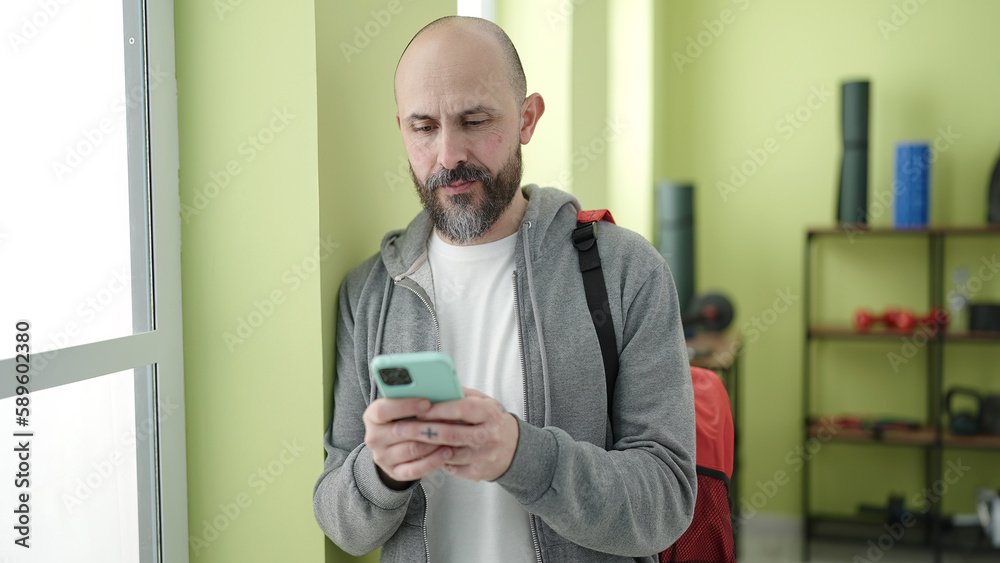 Young bald man using smartphone standing at sport center Young bald man using smartphone standing at sport center