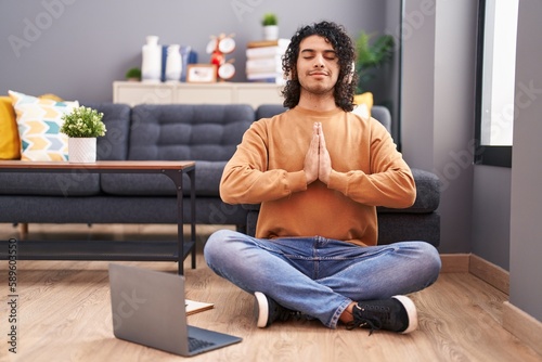Young latin man doing yoga exercise sitting on floor at home
