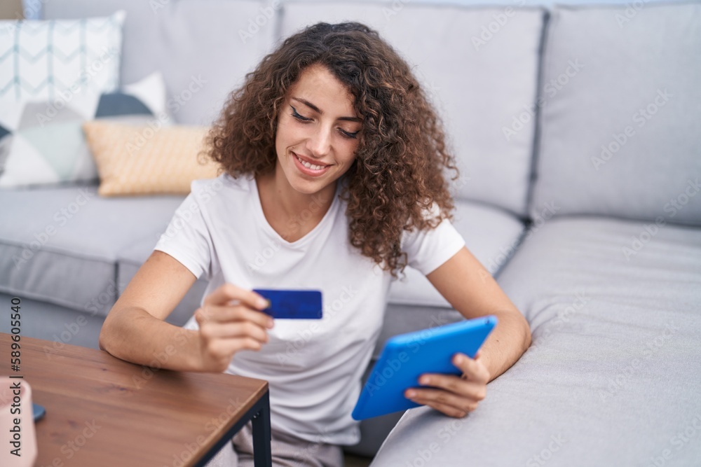 Young beautiful hispanic woman using touchpad and credit card sitting on floor at home Young beautiful hispanic woman using touchpad and credit card sitting on floor at home
