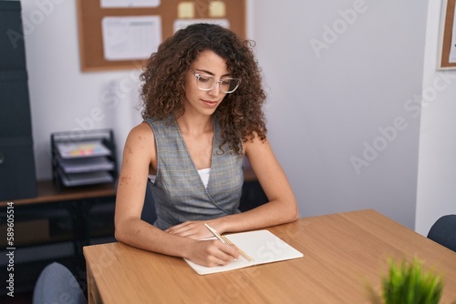 Young beautiful hispanic woman business worker writing on notebook working at office © Krakenimages.com