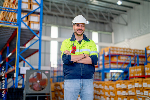 Professional warehouse worker stand with arm-crossed and smiling also look at camera stand in front of shelves with cardbox of product in workplace.
