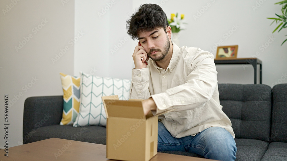 Young hispanic man speaking on the phone unpacking cardboard box at home Young hispanic man speaking on the phone unpacking cardboard box at home