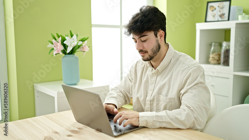 Young hispanic man using laptop sitting on table at dinning room