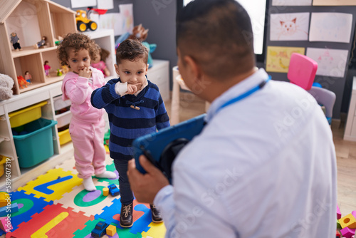 Hispanic man with boy and girl having lesson using touchpad at kindergarten