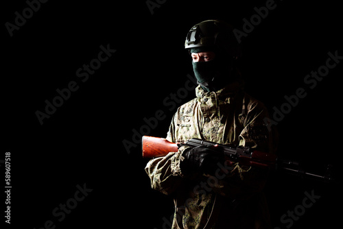 An armed soldier in military uniform holds a rifle in his hands on a black background, studio