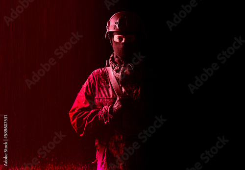 An armed soldier in military uniform holds a rifle in his hands on a black and red background, studio