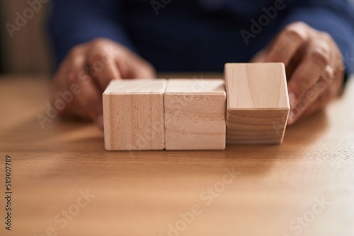 Young latin man business worker sitting on table with wooden cubes at office