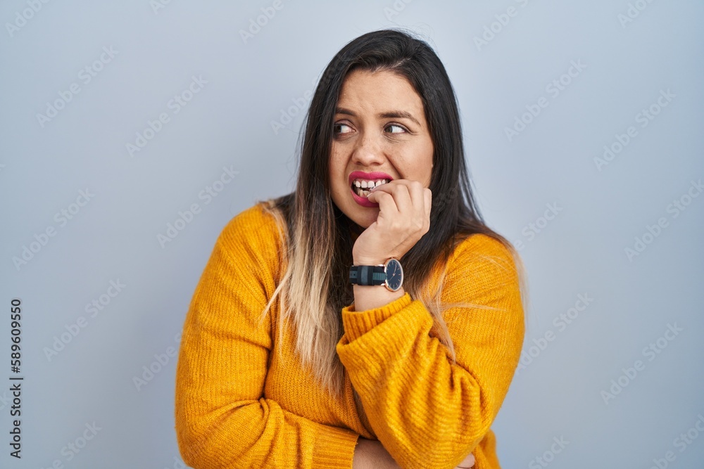 Young hispanic woman standing over isolated background looking stressed and nervous with hands on mouth biting nails. anxiety problem. Young hispanic woman standing over isolated background looking stressed and nervous with hands on mouth biting nails. anxiety problem.
