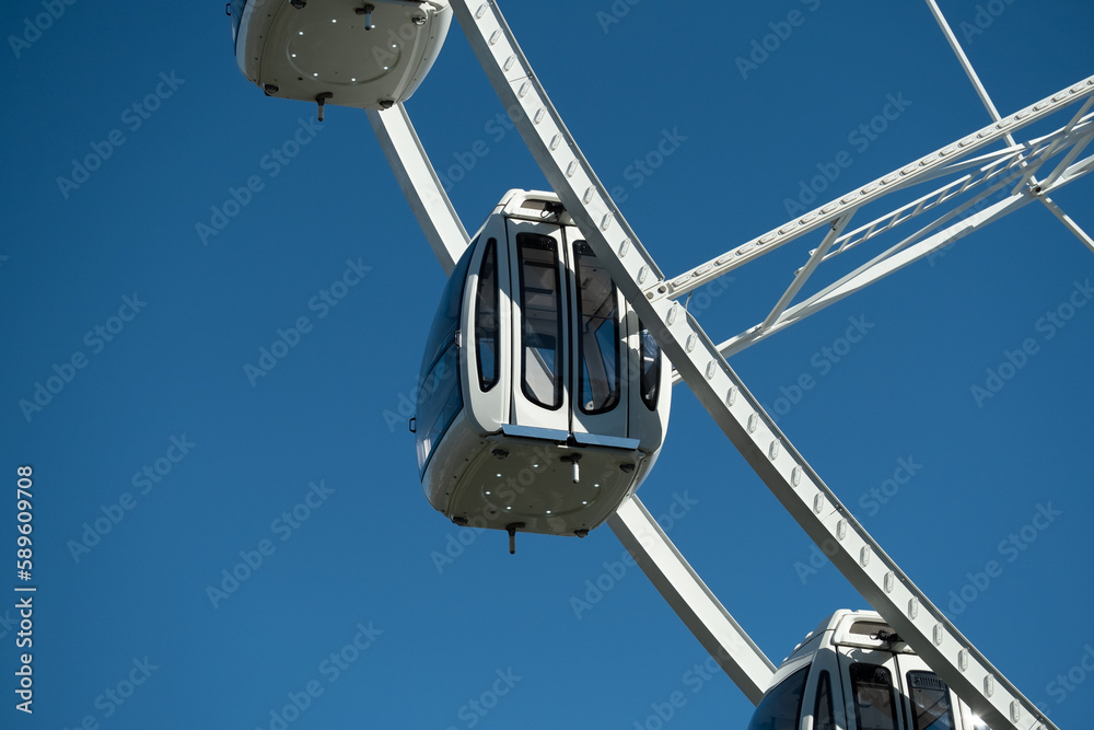 Fragment of the Ferris wheel. A white cabin against a blue sky.