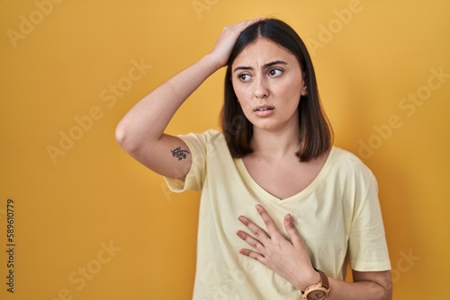 Hispanic girl wearing casual t shirt over yellow background touching forehead for illness and fever, flu and cold, virus sick