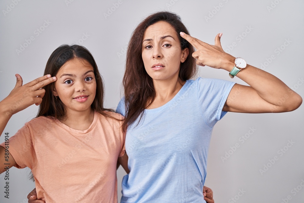 Young mother and daughter standing over white background shooting and killing oneself pointing hand and fingers to head like gun, suicide gesture. Young mother and daughter standing over white background shooting and killing oneself pointing hand and fingers to head like gun, suicide gesture.