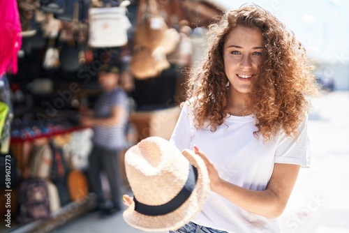 Young beautiful hispanic woman smiling confident holding hat at street market