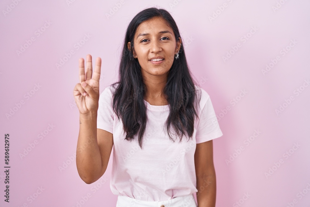 Young hispanic woman standing over pink background showing and pointing up with fingers number three while smiling confident and happy. Young hispanic woman standing over pink background showing and pointing up with fingers number three while smiling confident and happy.
