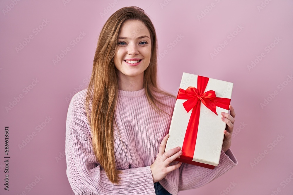 Young caucasian woman holding gift smiling with a happy and cool smile on face. showing teeth. Young caucasian woman holding gift smiling with a happy and cool smile on face. showing teeth.