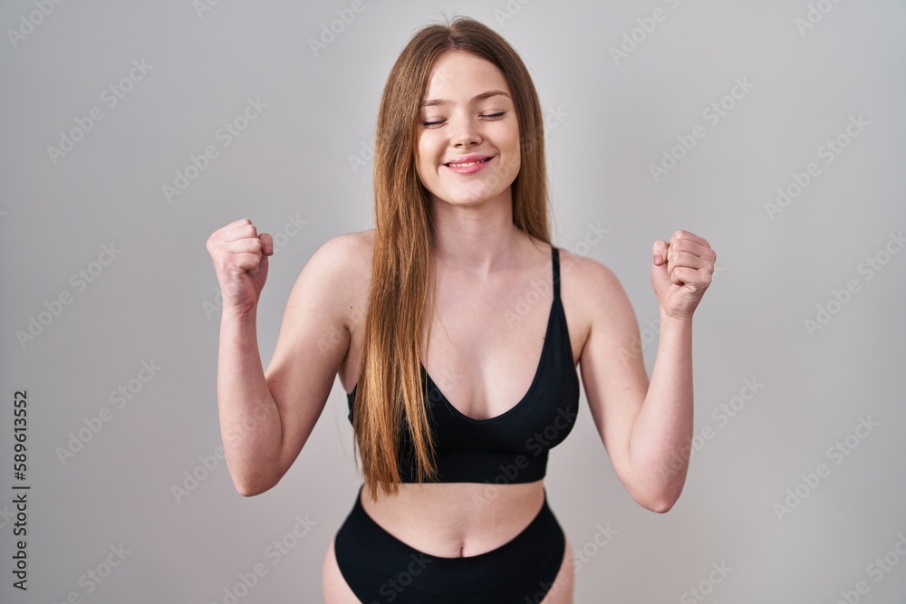 Young caucasian woman wearing lingerie excited for success with arms raised and eyes closed celebrating victory smiling. winner concept. Young caucasian woman wearing lingerie excited for success with arms raised and eyes closed celebrating victory smiling. winner concept.