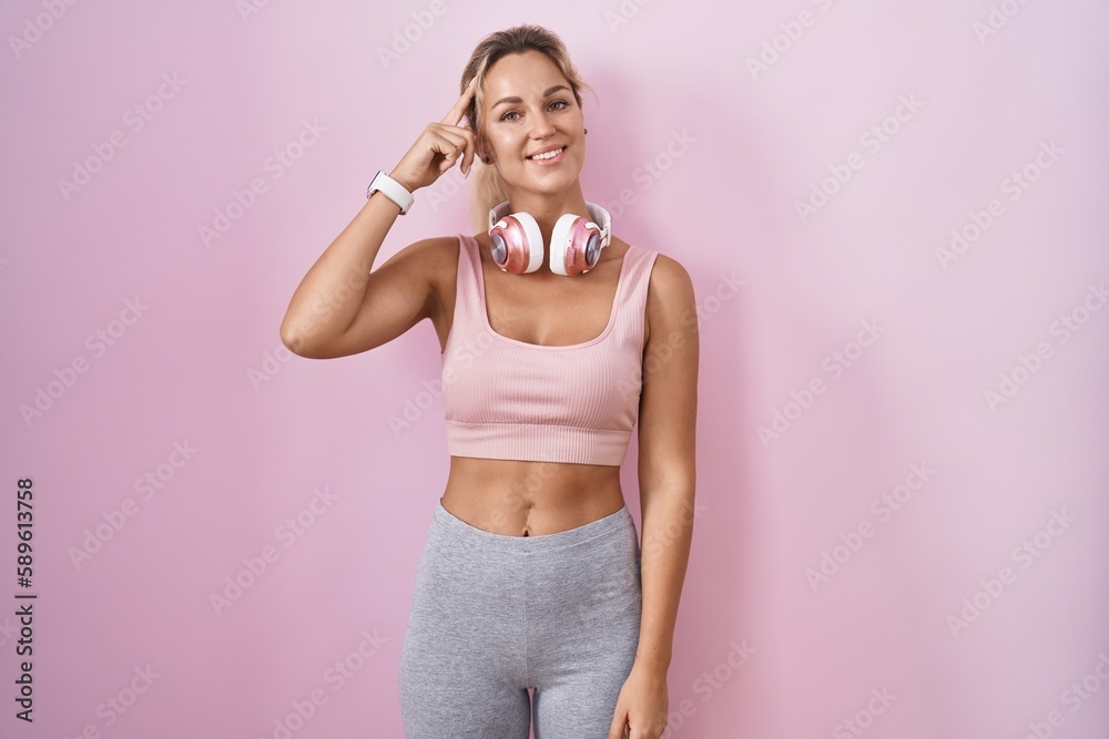 Young blonde woman wearing sportswear and headphones smiling pointing to head with one finger, great idea or thought, good memory