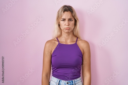 Young blonde woman standing over pink background depressed and worry for distress, crying angry and afraid. sad expression.
