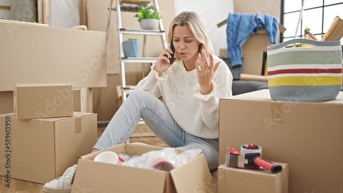 Young blonde woman talking on smartphone looking upset at new home