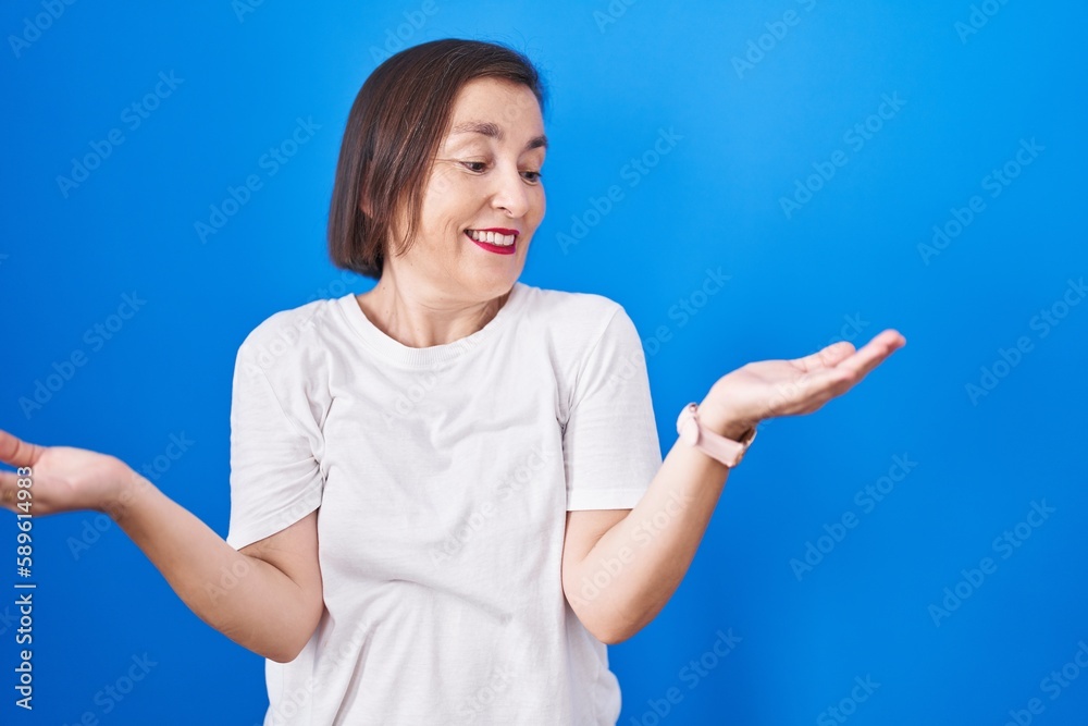 Middle age hispanic woman standing over blue background smiling showing both hands open palms, presenting and advertising comparison and balance Middle age hispanic woman standing over blue background smiling showing both hands open palms, presenting and advertising comparison and balance