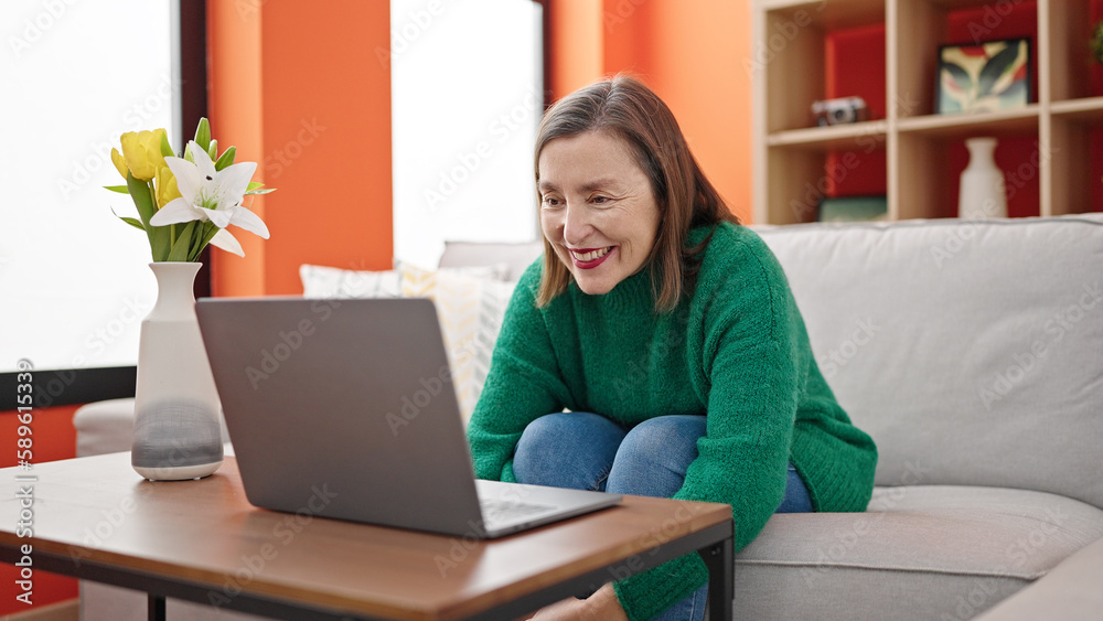 Mature hispanic woman with grey hair using laptop sitting on sofa at home Mature hispanic woman with grey hair using laptop sitting on sofa at home